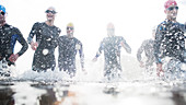 Triathletes in wetsuits running in waves