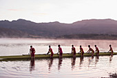 Rowing crew placing scull in lake at dawn