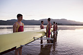 Rowing team holding scull in lake at dawn
