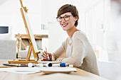Smiling woman painting at easel on table