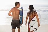 Couple walking with surfboards on beach