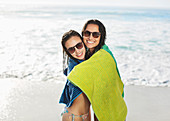 Smiling friends wrapped in towel on beach