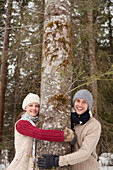 Couple hugging tree trunk in woods