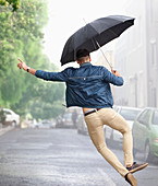 Man dancing with umbrella in rainy street