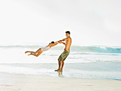 Father swinging daughter on beach