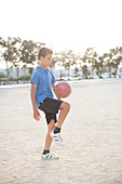 Boy kneeing soccer ball in sand