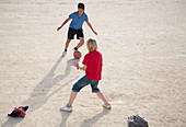 Boys playing with soccer ball in sand