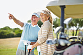 Senior couple standing next to golf cart