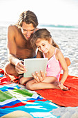 Father and daughter using tablet on beach