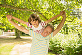 Father piggybacking son under tree