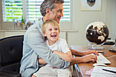 Father holding son and using computer