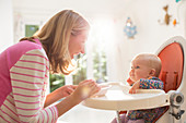 Mother feeding baby girl in high chair