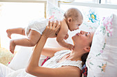 Mother playing with baby boy on bed