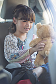 Girl with teddy bear in back seat of car
