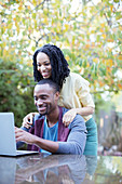 Happy couple using laptop at patio table