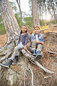 Children sitting on tree roots in forest