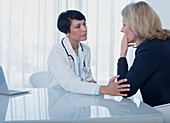 Female doctor consoling sad woman at desk