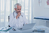 Smiling mature doctor at desk with laptop