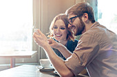 Couple using cell phone in sunny cafe