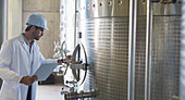 Vintner in lab coat and hard hat examining stainless steel v