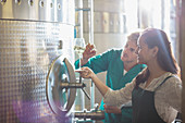 Vintners examining white wine at stainless steel vat