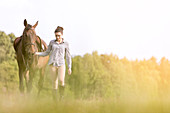 Woman walking horse in rural field