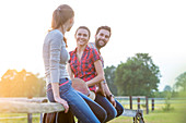 Smiling friends sitting on rural fence