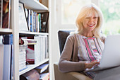 Smiling senior woman using laptop in den