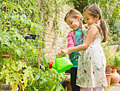 Hugging girls watering plants in garden