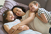 Mother and daughters cuddling on sofa