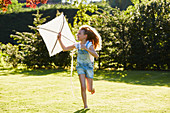 Girl running with kite in sunny garden