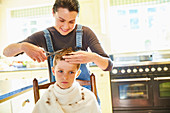 Unhappy boy getting haircut from mother