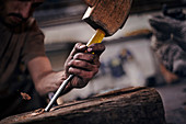 Blacksmith chiselling wood with tool