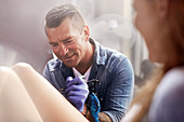 Tattoo artist tattooing woman's leg