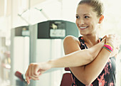 Smiling woman stretching arm at gym