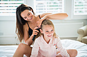Mother brushing daughter's hair on bed