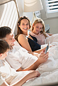 Family relaxing with tablet in bed