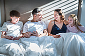 Smiling family laying in bed using tablet
