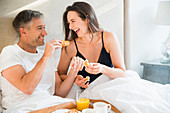 Laughing couple enjoying breakfast in bed