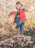 Boy jumping over pile of autumn leaves