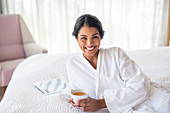Woman in bathrobe drinking tea on bed