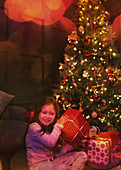 Girl shaking gift at Christmas tree