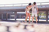 Boy teaching girlfriend skateboarding
