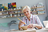 Mature woman painting pottery bowl