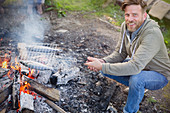 Smiling man cooking fish over campfire