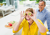 Mature woman covering eyes with kiwi slices