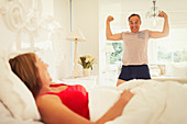 Mature man flexing muscles for wife in bedroom