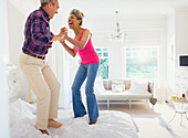 Playful mature couple jumping on top of bed