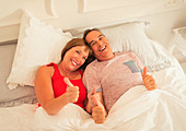 Mature couple gesturing thumbs-up in bed