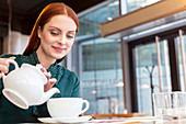 Smiling woman pouring tea in cafe